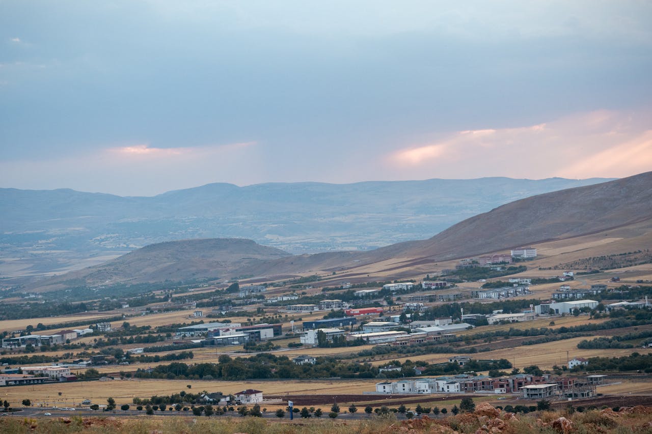 hero-img-01 A serene view of Elazigs countryside with hills and fields under a pastel sky at dusk.