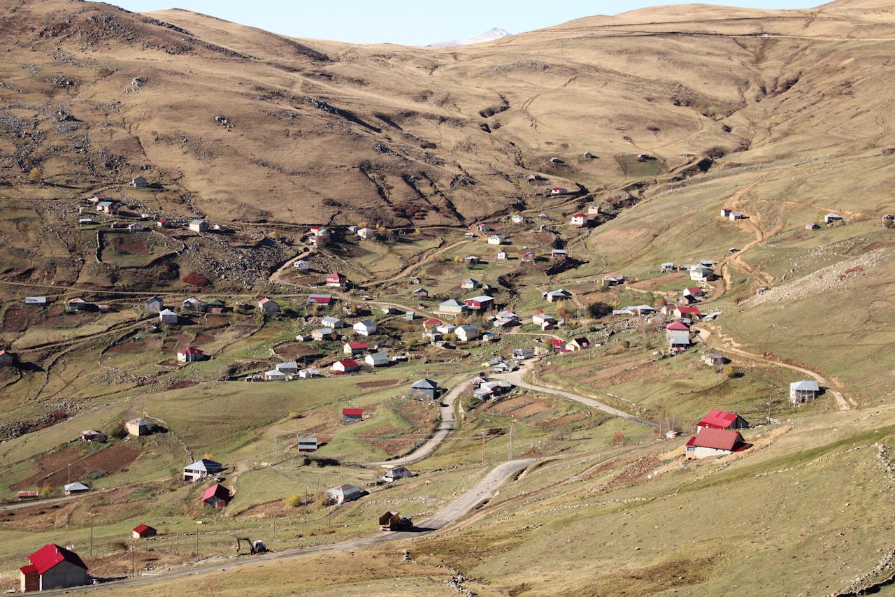 why-choose-us Aerial view of a rural mountain village with scattered homes and winding roads.